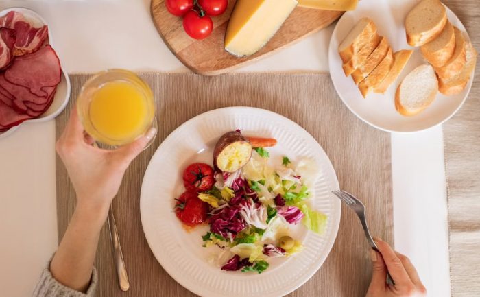 A top-view of a delicious breakfast setting featuring a salad, bread, cheese, tomatoes, and orange juice.