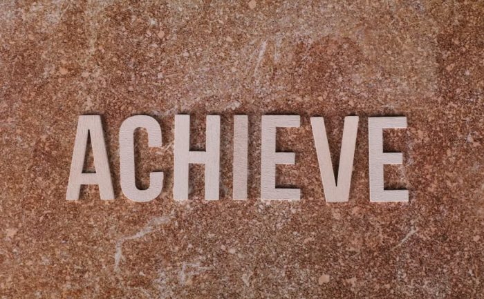 Wooden letters spelling 'ACHIEVE' on a textured brown surface, conveying motivation and success.